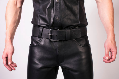 Person wearing a black leather outfit with a belt on a plain background