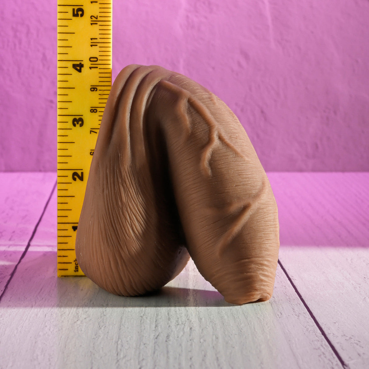 Gender X Uncircumcised Packer, Dark, next to a ruler for scale